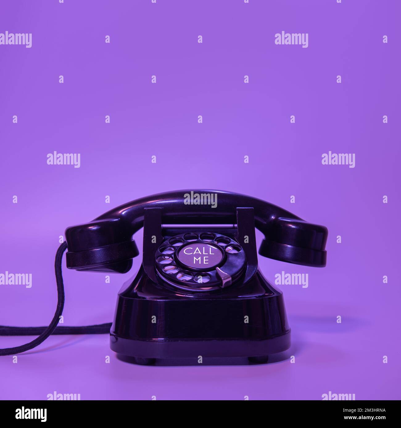 Vecchio telefono nero su sfondo viola. con un'iscrizione - chiamami Foto Stock