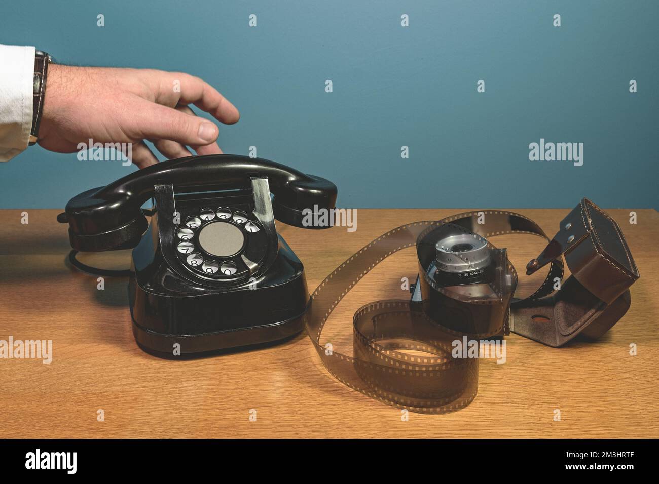 La mano raccoglie il ricevitore un vecchio apparecchio telefonico su un tavolo di legno, una pellicola, una telecamera. sfondo blu Foto Stock