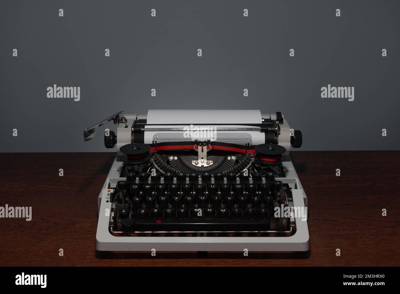 Macchina da scrivere 70s con nastro stampato rosso senza coperchio superiore su tavolo di legno e sfondo grigio Foto Stock