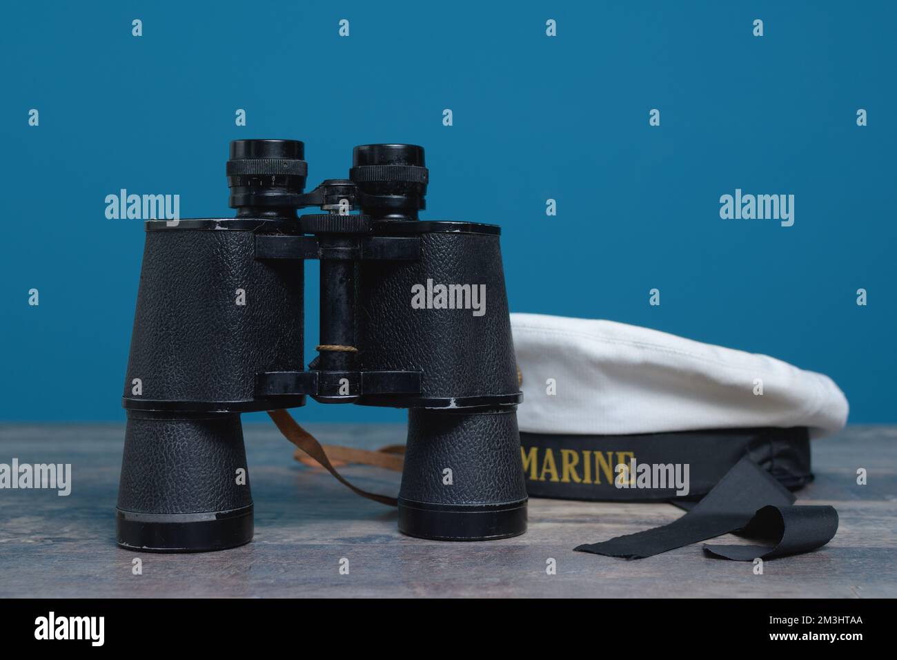 Vecchio binocolo marino e berretto senza cappuccio su sfondo turchese su un tavolo di legno testurizzato Foto Stock