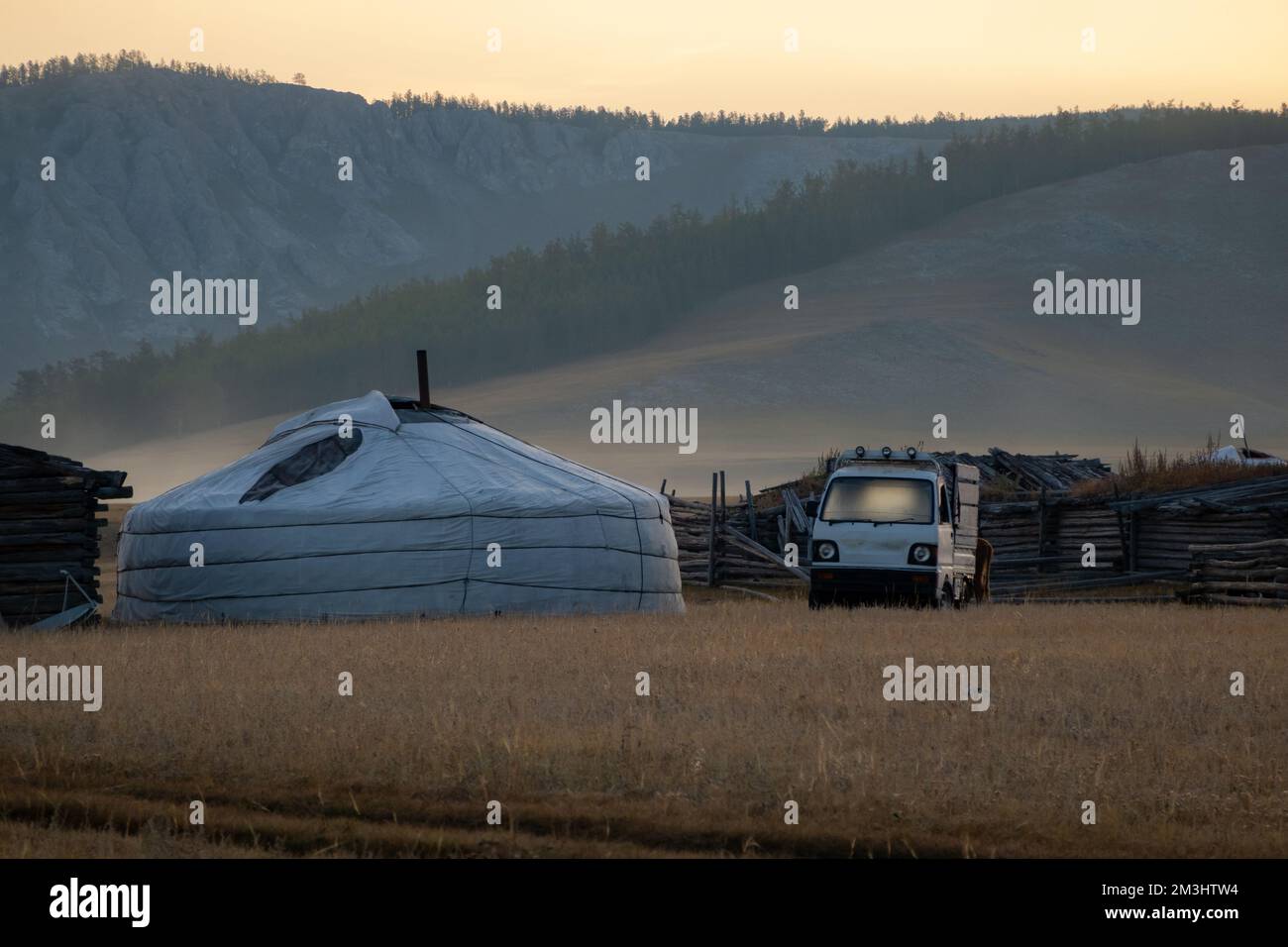 Yurt nomade in campagna con le montagne sullo sfondo in una serata di sole. Tenda GER nel paese rurale circondato da boschi e colline, Foto Stock