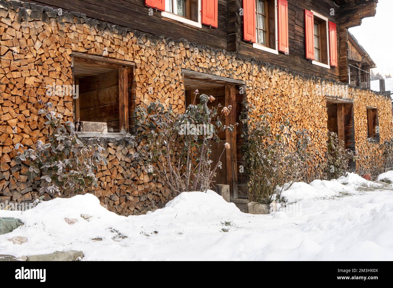 legna da ardere impilata sulla parete esterna di una tradizionale casa alpina in inverno Foto Stock