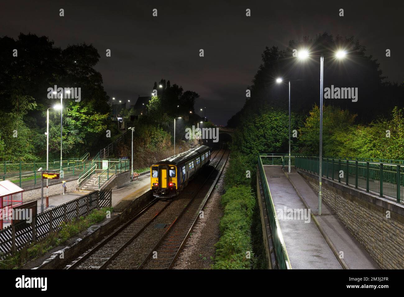 Stazione ferroviaria di Woodlesford, Yorkshire, Regno Unito. Un treno velocissimo di classe 150 della ferrovia del Nord chiama in una notte bagnata al buio Foto Stock