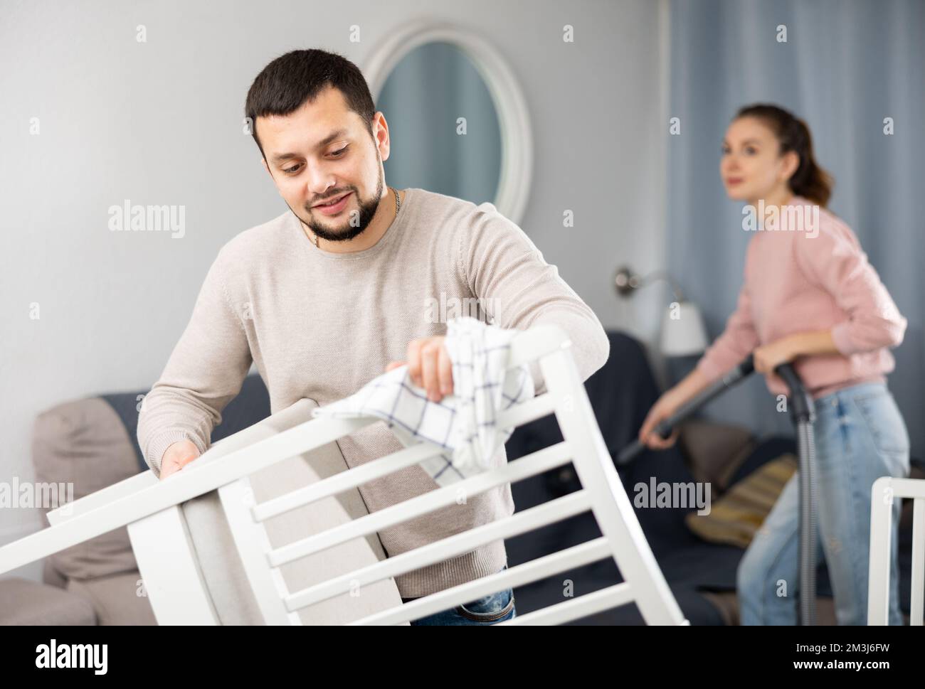 Giovane uomo che puliva i mobili mentre la ragazza aspira il divano Foto Stock