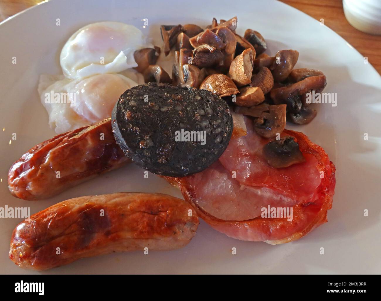 Colazione completa fritta, funghi, pancetta, salsicce, uova in camicia, pudding nero, su un piatto Foto Stock