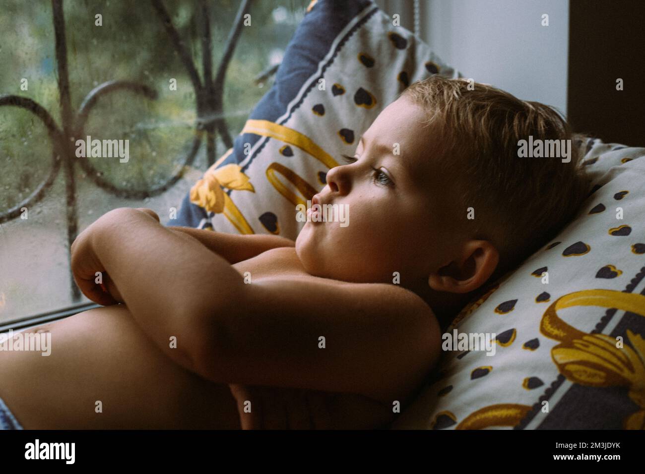 il bambino guarda la pioggia fuori dalla finestra Foto Stock