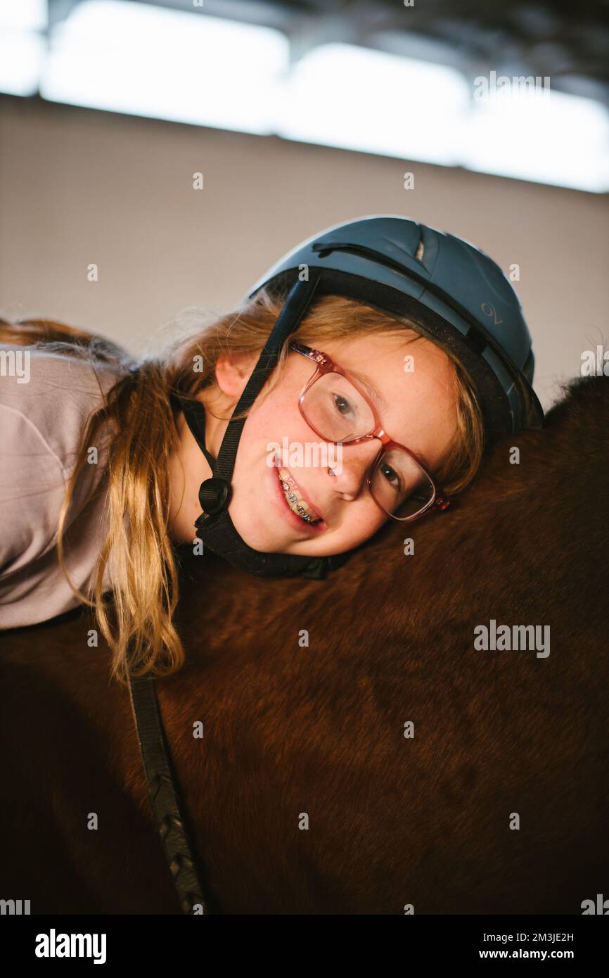 Ragazza con occhiali e bretelle sorride in casco a cavallo Foto Stock