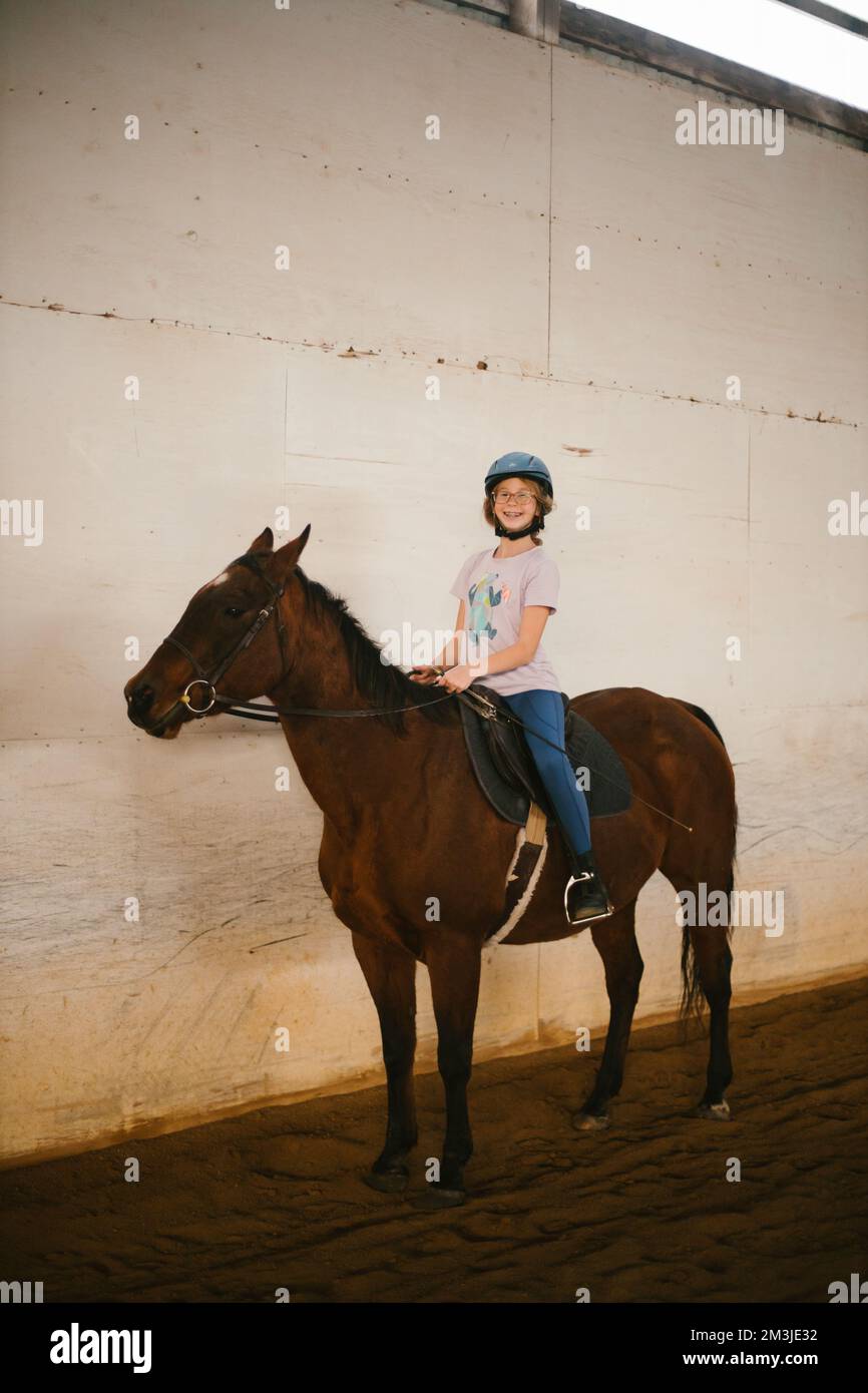 Ragazza felice su pony marrone per la lezione di equitazione a cavallo nel fienile Foto Stock