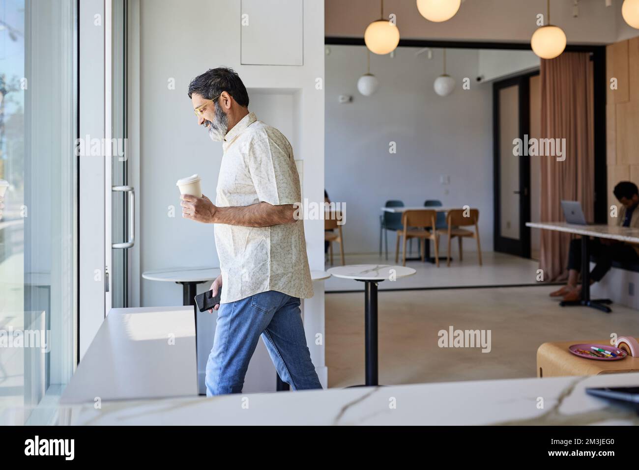 Uomo maturo sorridente con una tazza da caffè usa e getta che lascia la caffetteria Foto Stock