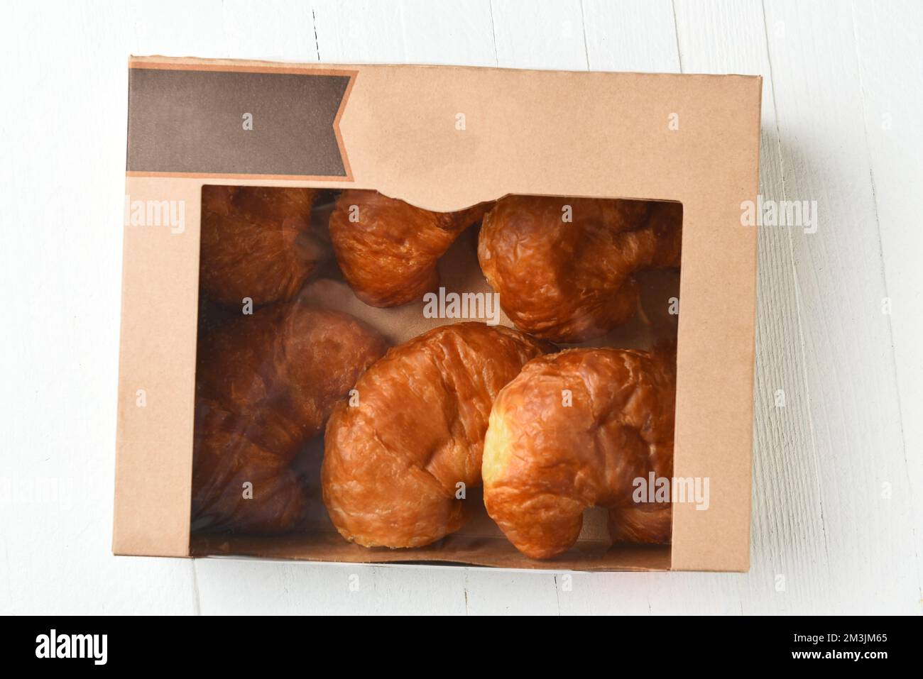 Sei croissant panini in una scatola da forno, su un rustico tavolo di legno bianco. Foto Stock