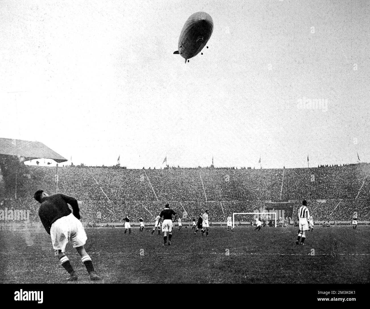 Stadio di Wembley, durante la città di Huddersfield contro l'Arsenal F.A. Coppa finale del 1930, con il 'Graf Zeppelin' nel cielo sopra. Si è riferito che il velivolo tedesco "si è mantenuto molto basso a terra, sconcertando giocatori e spettatori con il ruggito assordante dei suoi motori”. Arsenal ha vinto la partita 2-0. Data: 1930 Foto Stock