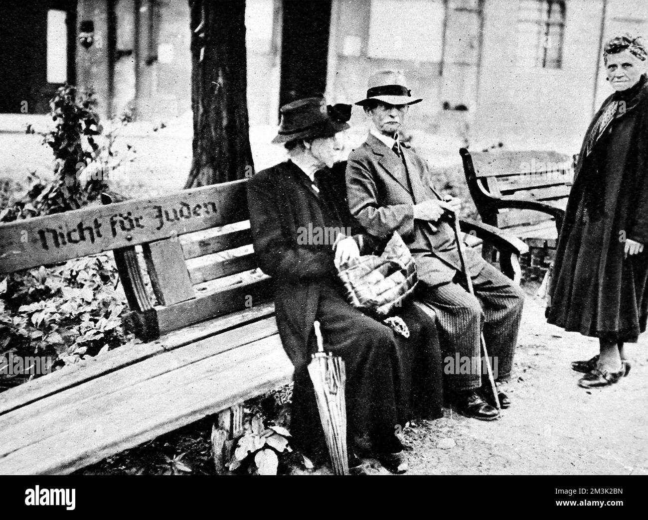 Due cittadini di Berlino seduti su un banco pubblico segnato con la leggenda "Nicht fur Juden" (non per ebrei), Berlino, 1945. Questa reliquia dello stato nazista antisemita (1933-45) riuscì a sopravvivere a tutti i bombardamenti e i combattimenti di Berlino durante la seconda guerra mondiale. 1945 Foto Stock