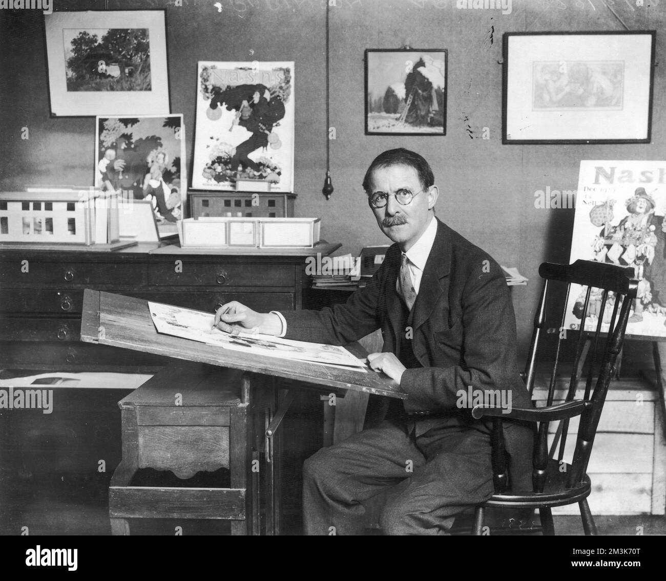 WILLIAM HEATH ROBINSON (1872 - 1944), artista e illustratore, ha mostrato di lavorare nel suo studio. La prolifica carriera di Heath Robinson si è protratta per cinque decenni. Durante questo periodo, ha prodotto innumerevoli illustrazioni per The Sketch e The Bystander e per altre riviste ILN. Egli è citato come dicendo, 'sono stato abbastanza lanciato sulla mia carriera' della decisione di Bruce Ingram di pubblicare le sue illustrazioni in The Sketch nel marzo 1906. È meglio conosciuto per le sue ingegnose contrazioni, ma il suo lavoro si è esteso ai temi del golf, del cricket, della guerra, del giardinaggio e altro ancora. Foto Stock