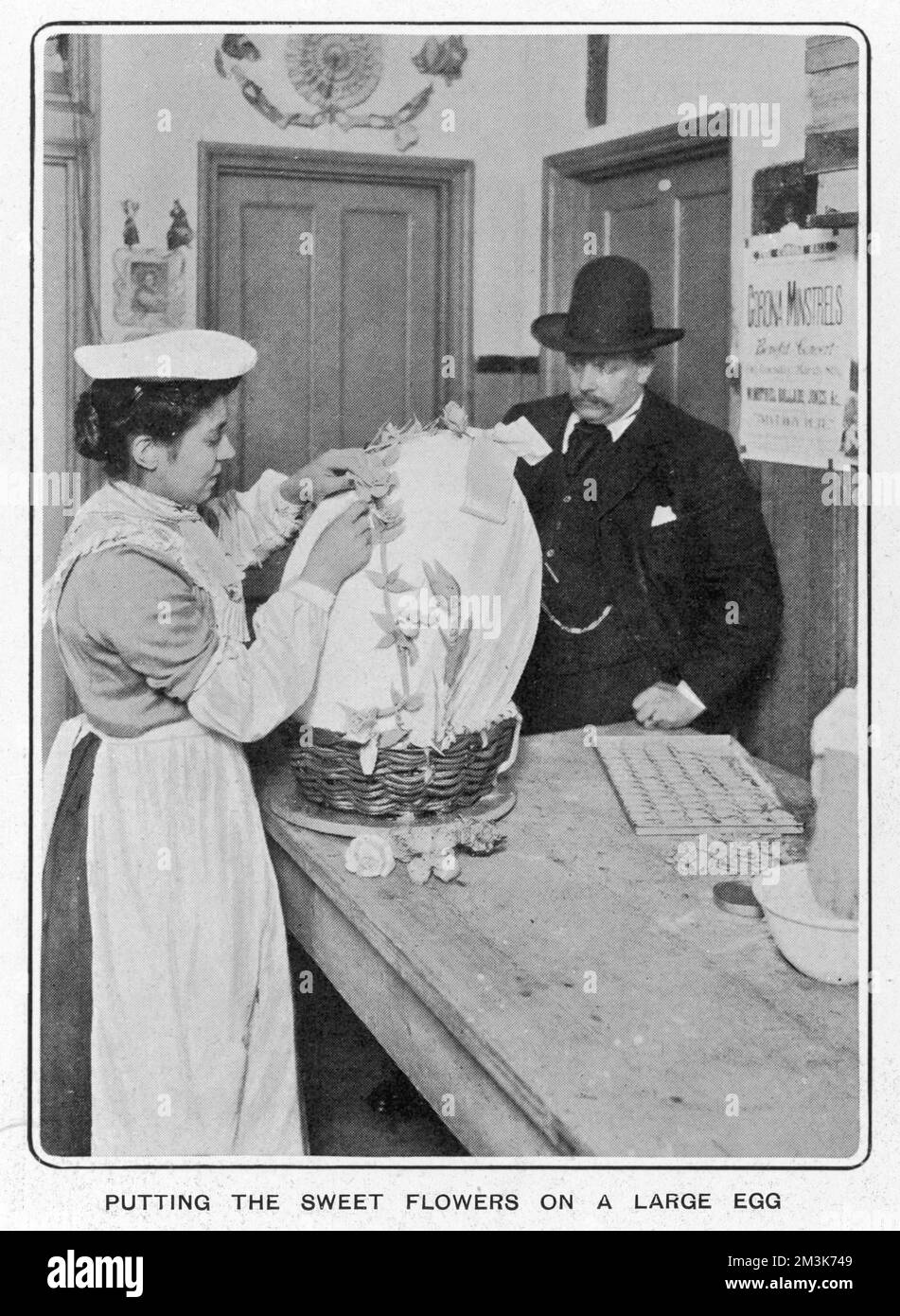 Un lavoratore che mette fiori dolci su un grande uovo di Pasqua al cioccolato presso Fuller's Confections Factory. Data: 1904 Foto Stock