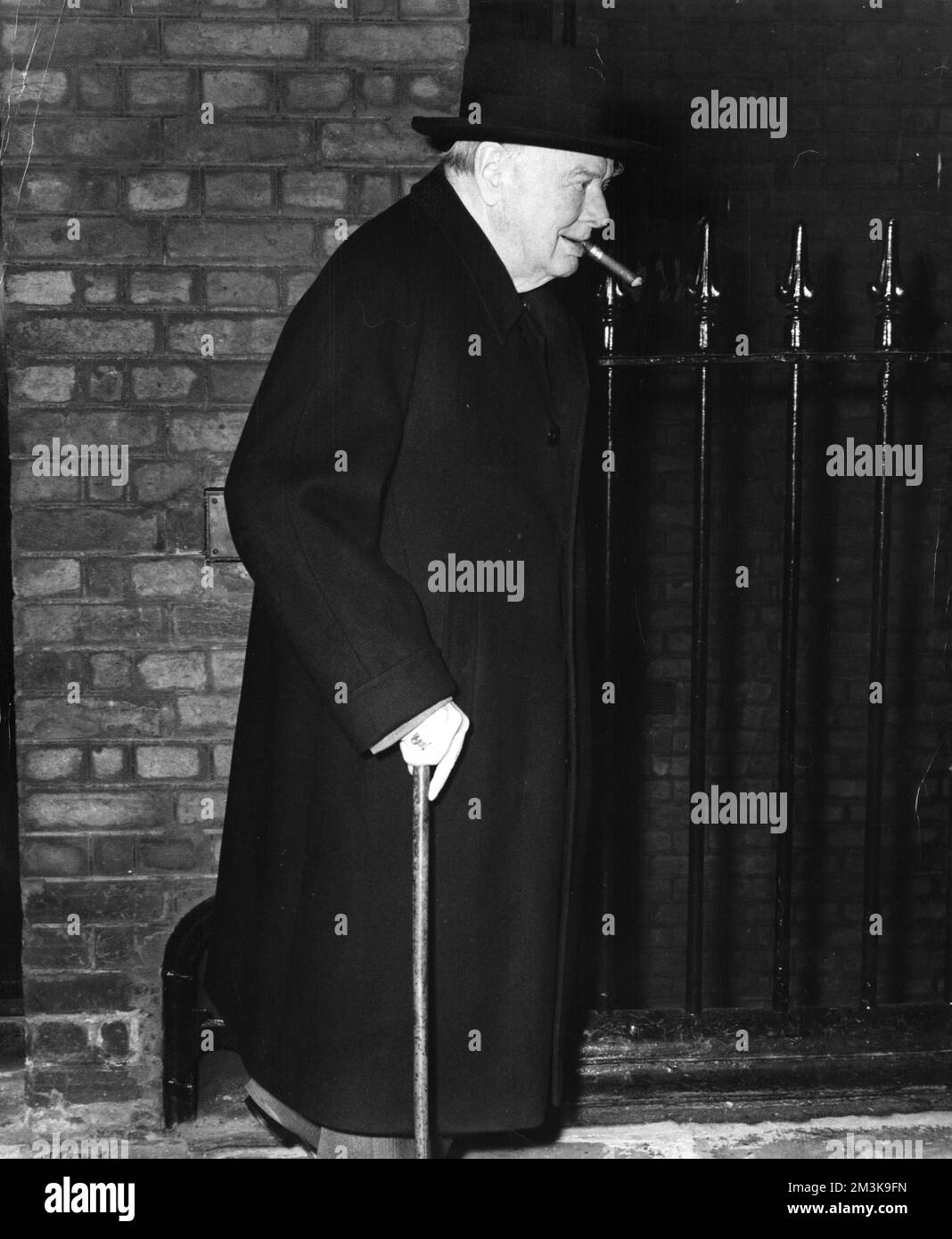 Sir Winston Leonard Spencer Churchill (1874-1965) politico e primo ministro britannico fumando un sigaro con un bastone che lascia la sua residenza londinese per Chartwell tre giorni prima del suo 85th° compleanno Data: 27th novembre 1959 Foto Stock