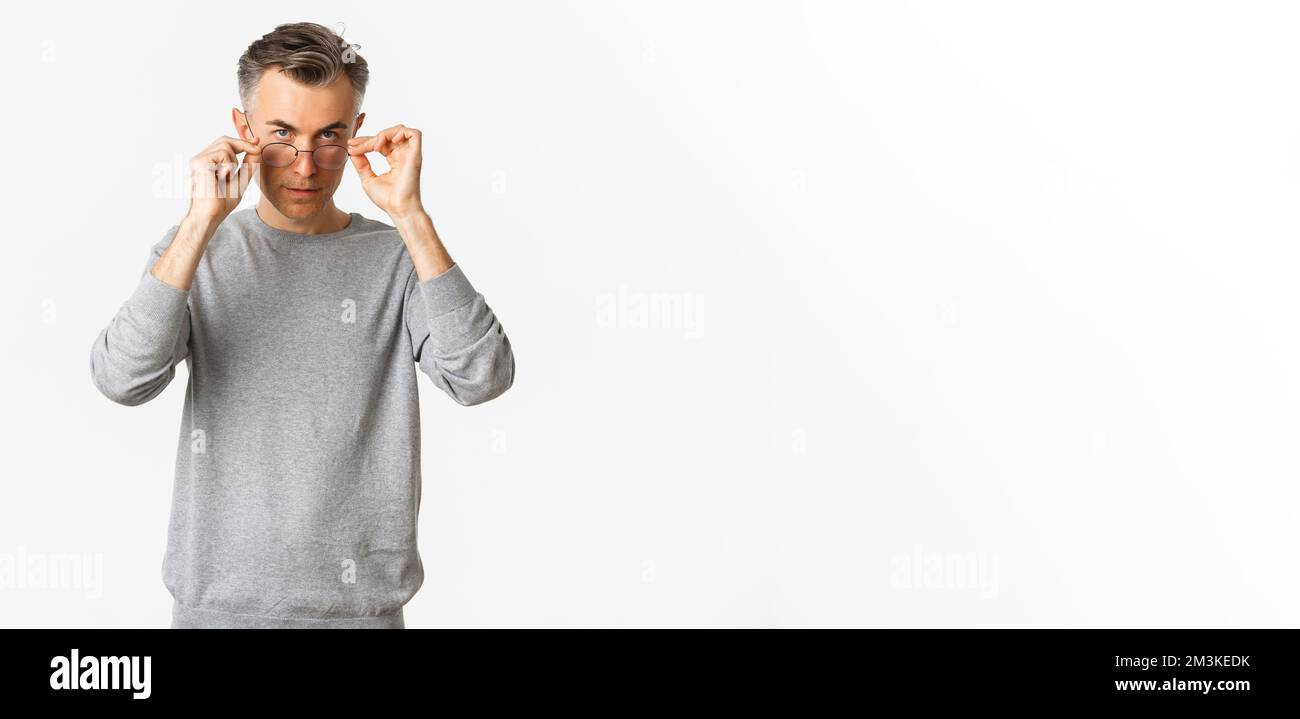 Immagine di un uomo di mezza età bello e sicuro con capelli corti grigi, indossati su occhiali e guardando serio la macchina fotografica, in piedi su sfondo bianco Foto Stock