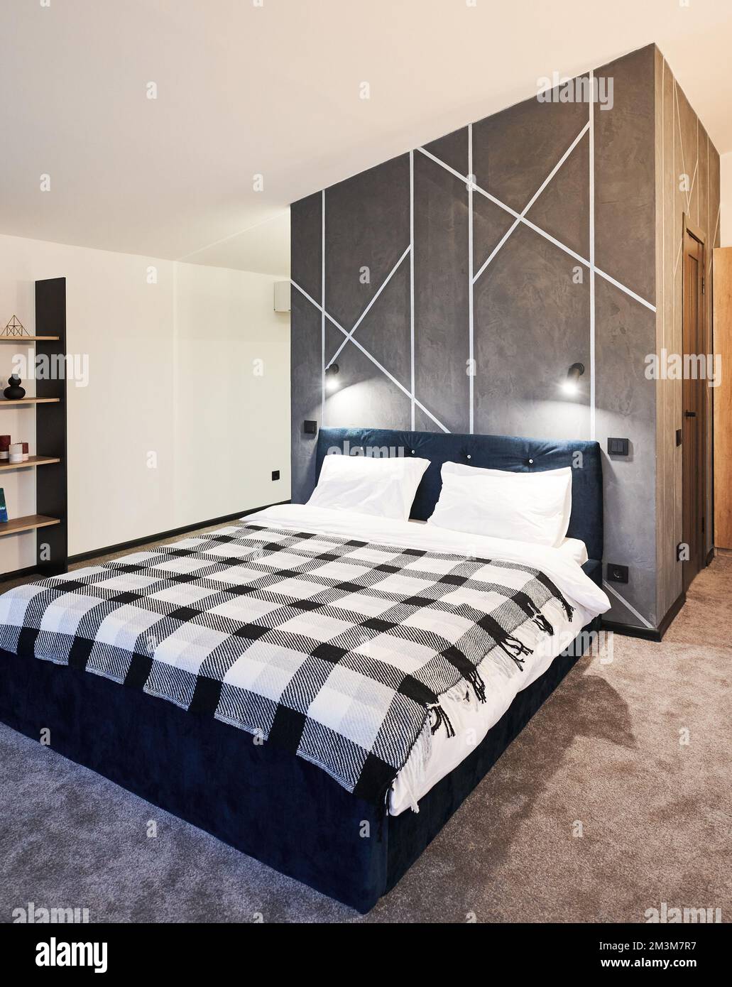 Interni minimalisti della camera da letto con grande letto interno. Vista frontale di ampio letto, con coperta a plaid contro parete grigia con ornamento geometrico nella zona notte. Concetto di interni. Foto Stock