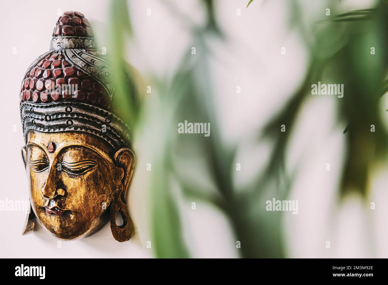 Primo piano di souvenir realizzati a mano maschera di buddha dorato su sfondo bianco sotto rami. Dettagli Foto Stock