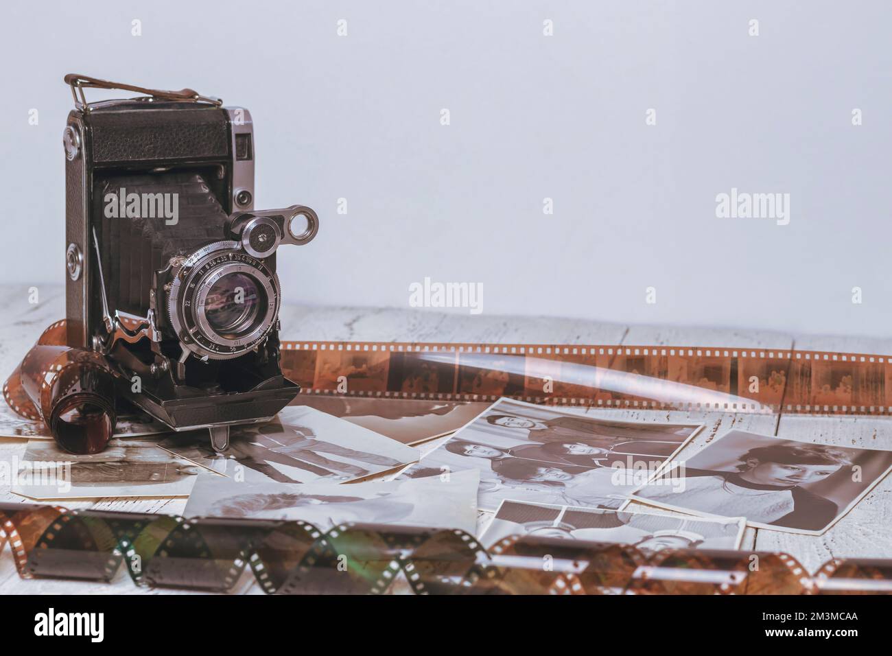 Un'antica macchina fotografica si erge su un tavolo di legno tra film fotografici e fotografie. Foto Stock
