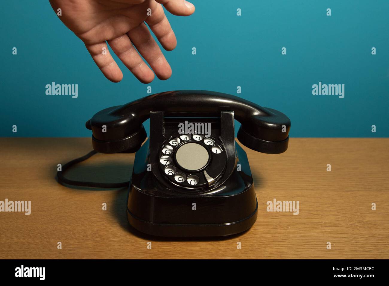 la mano raggiunge il vecchio telefono. Vecchio apparecchio telefonico su un tavolo di legno, installazione retrò. Spazio di copia Foto Stock