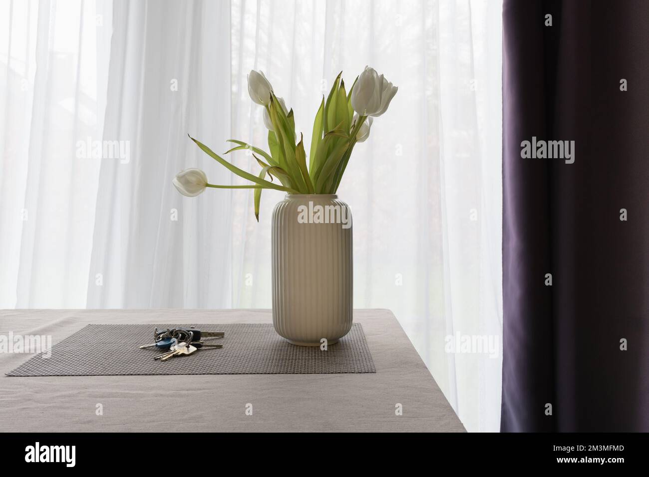 I fiori si appassiscono in un vaso e le chiavi lasciate sul tavolo. Foto Stock