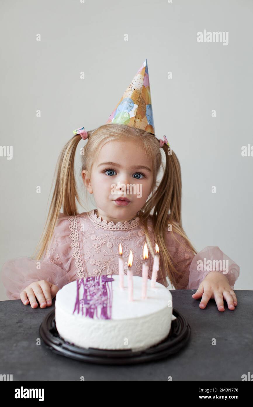 Bambina che festeggia il compleanno. Biondo con lunghe code di capelli il bambino soffia le candele sulla torta di compleanno Foto Stock