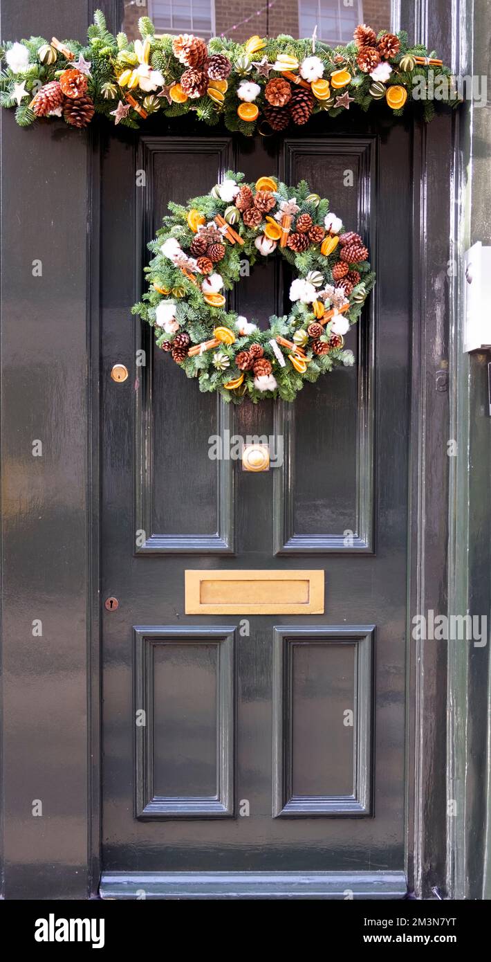 Bella corona di abete rosso di Natale con coni di pino bastoncini di cannella e decorazioni a fette arancioni appesi alla porta verde Londra Inghilterra UK KATHY DEWITT Foto Stock