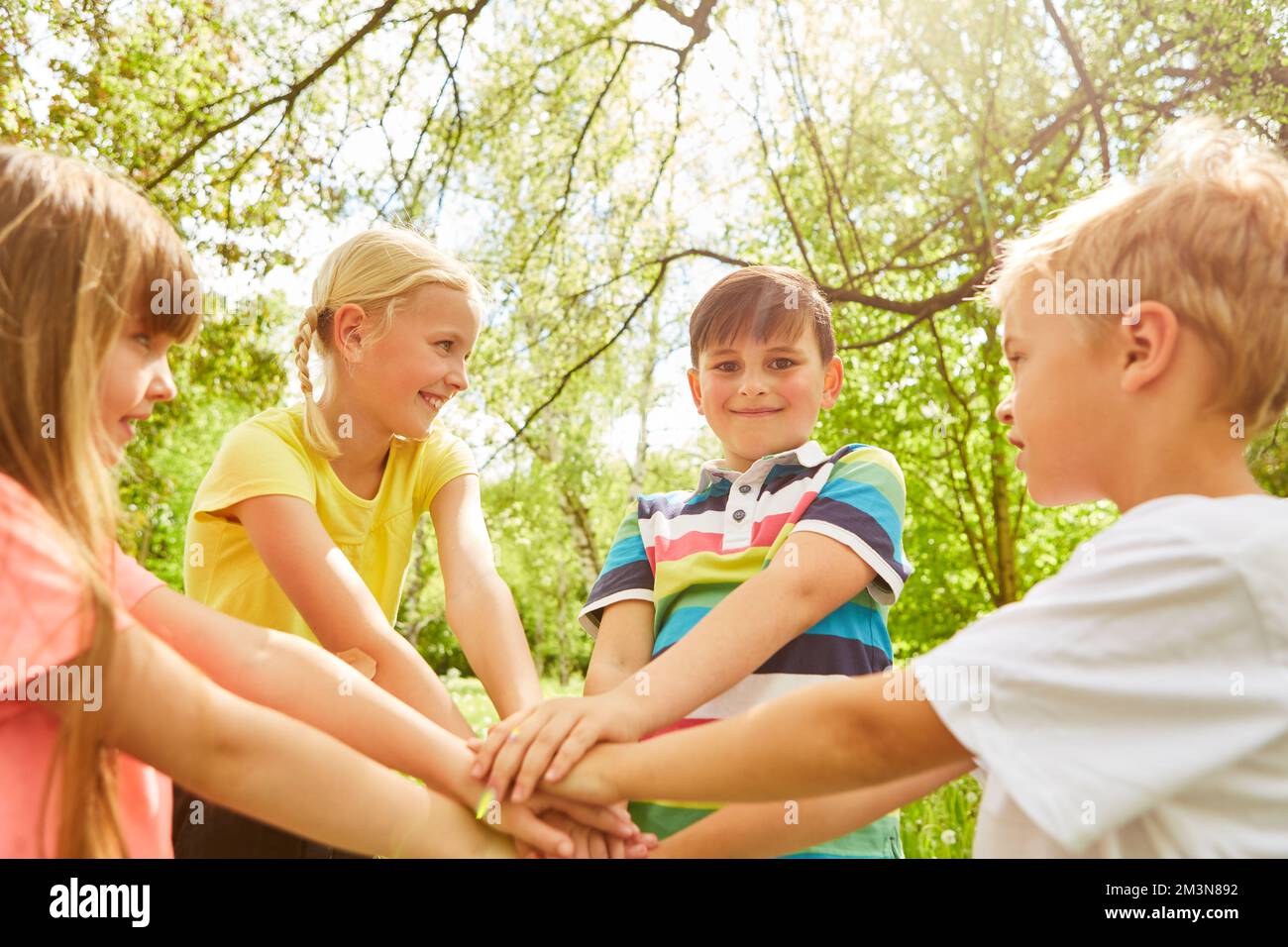 Amici elementari multirazziali con mani impilate che giocano in giardino durante le vacanze estive Foto Stock