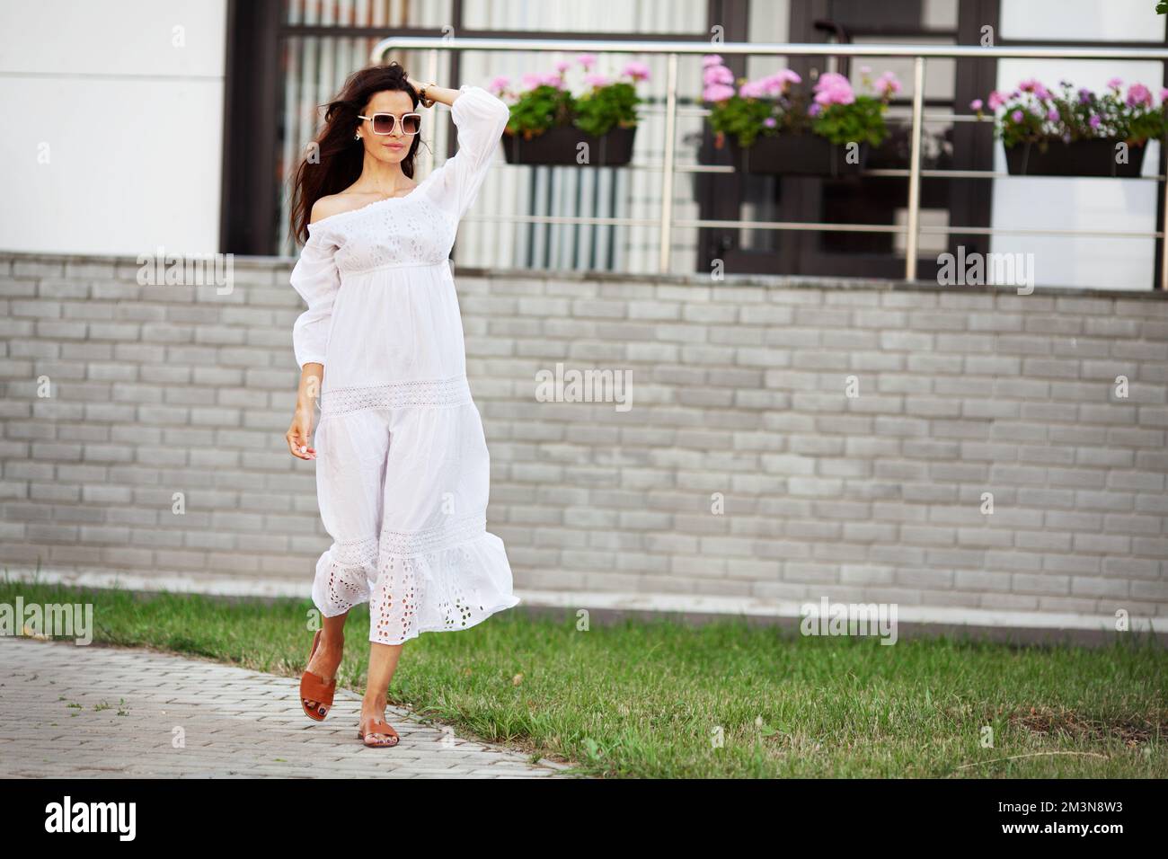 Donna che cammina. Bel modello che indossa abiti estivi alla moda e occhiali da sole bianchi Foto Stock
