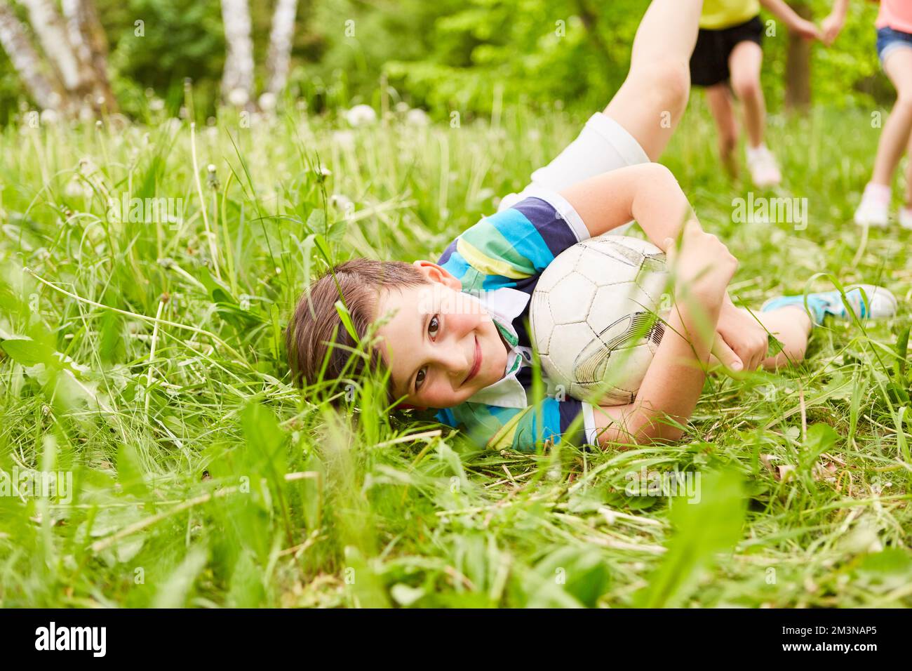 Ritratto di ragazzo sorridente con calcio sdraiato sull'erba in giardino durante le vacanze estive Foto Stock