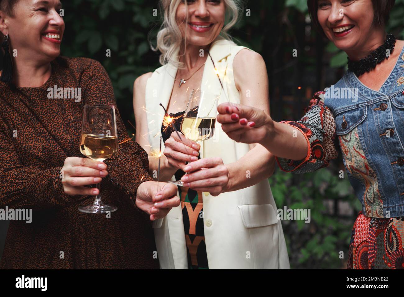 Felice donne mature amici celebrare il nuovo anno e ridere, tenere scintillanti e clink bicchieri di vino alcolico o champagne alla festa Foto Stock