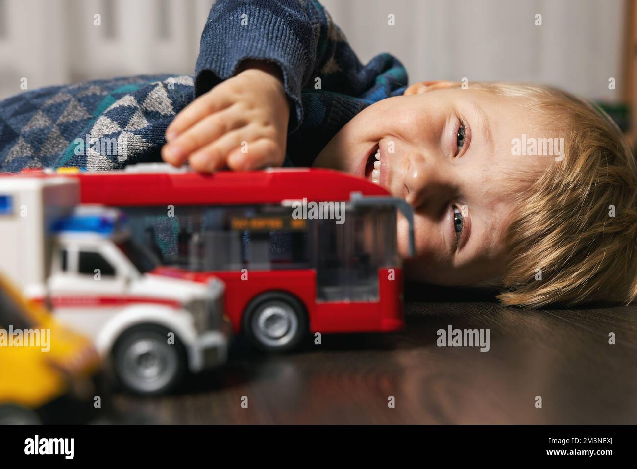 ragazzino che gioca con le auto giocattolo sul pavimento a casa Foto Stock