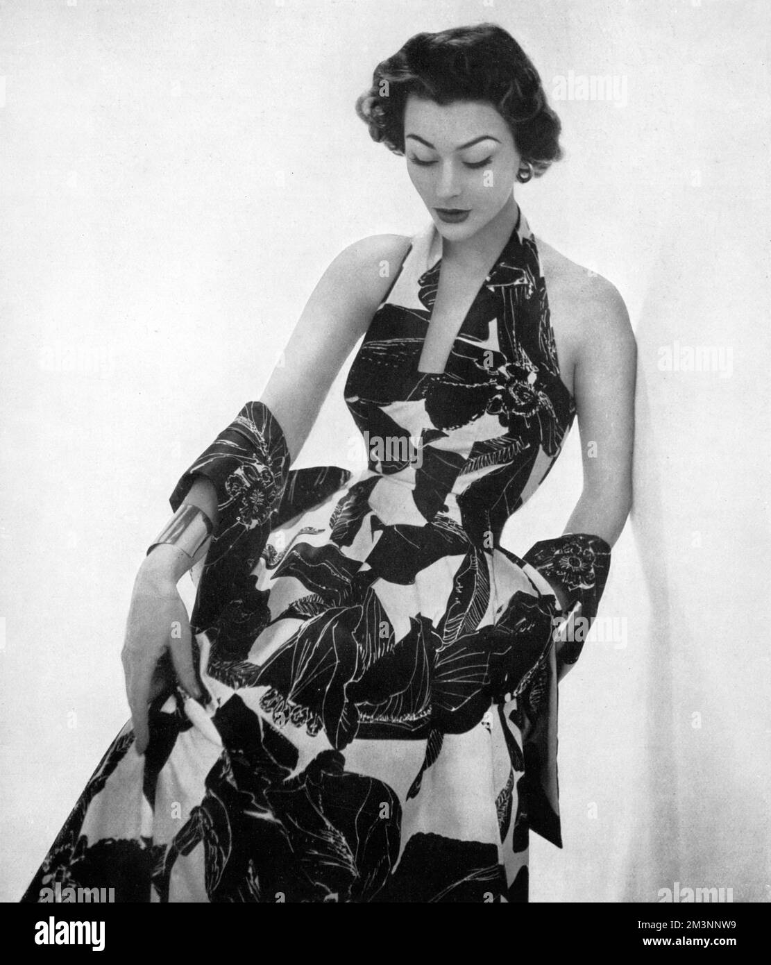 Un abito da sera con un collo a balze e una gonna piena e vorticosa in cotone smalto con stampa floreale tropicale. Data: 1953 Foto Stock
