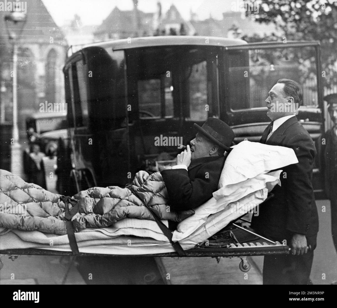 Profilo di Winston Churchill (1874-1965), politico inglese, avendo un puff cheeky sul suo sigaro mentre è teso dal suo appartamento di Londra ad una casa di cura del West End via ambulanza, essendo stato preso ammalato con paratifoide. Data: 1932 Foto Stock