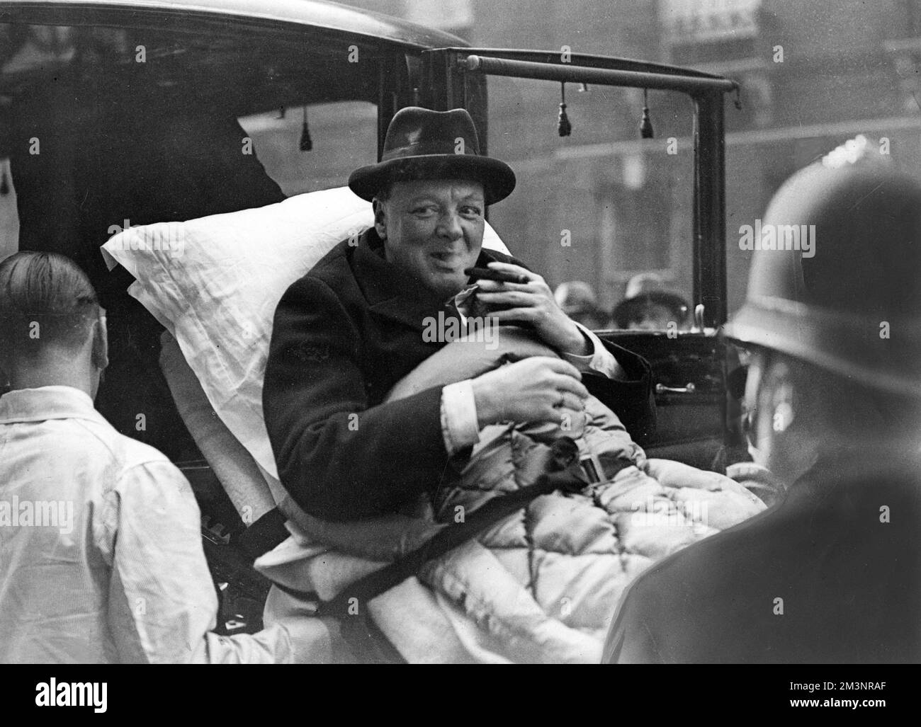 Winston Churchill (1874-1965), politico inglese, avendo un puff cheeky sul suo sigaro mentre è teso dal suo appartamento londinese ad una casa di cura del West End via ambulanza, essendo stato preso ammalato di paratifoid. Data: 1932 Foto Stock