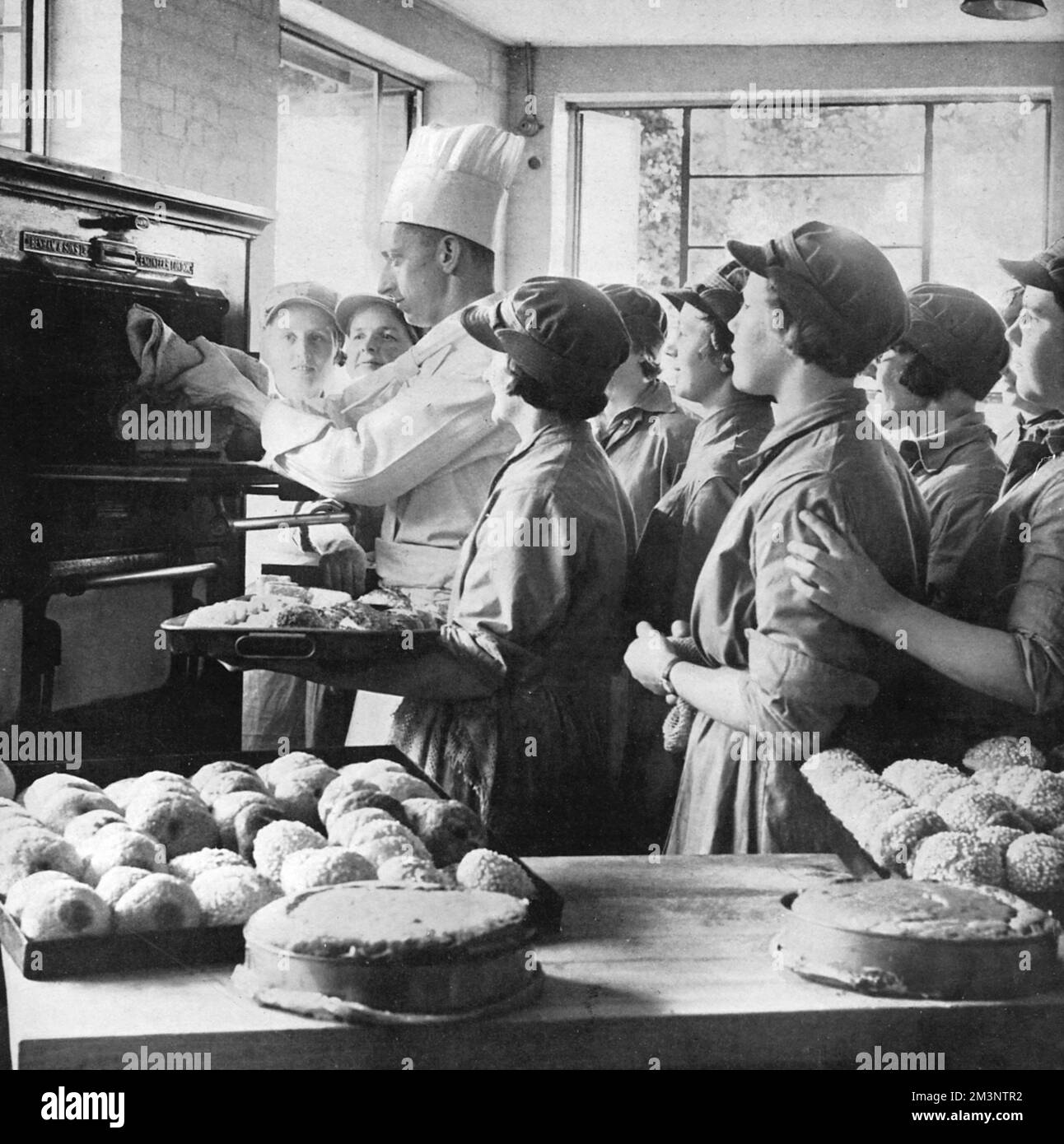 Un istruttore che mostra alle lavoratrici ATS come regolare i forni da cucina per ottenere torte e panini appetitosi per le nuove truppe nelle prime settimane della seconda guerra mondiale Data: 1939 Foto Stock