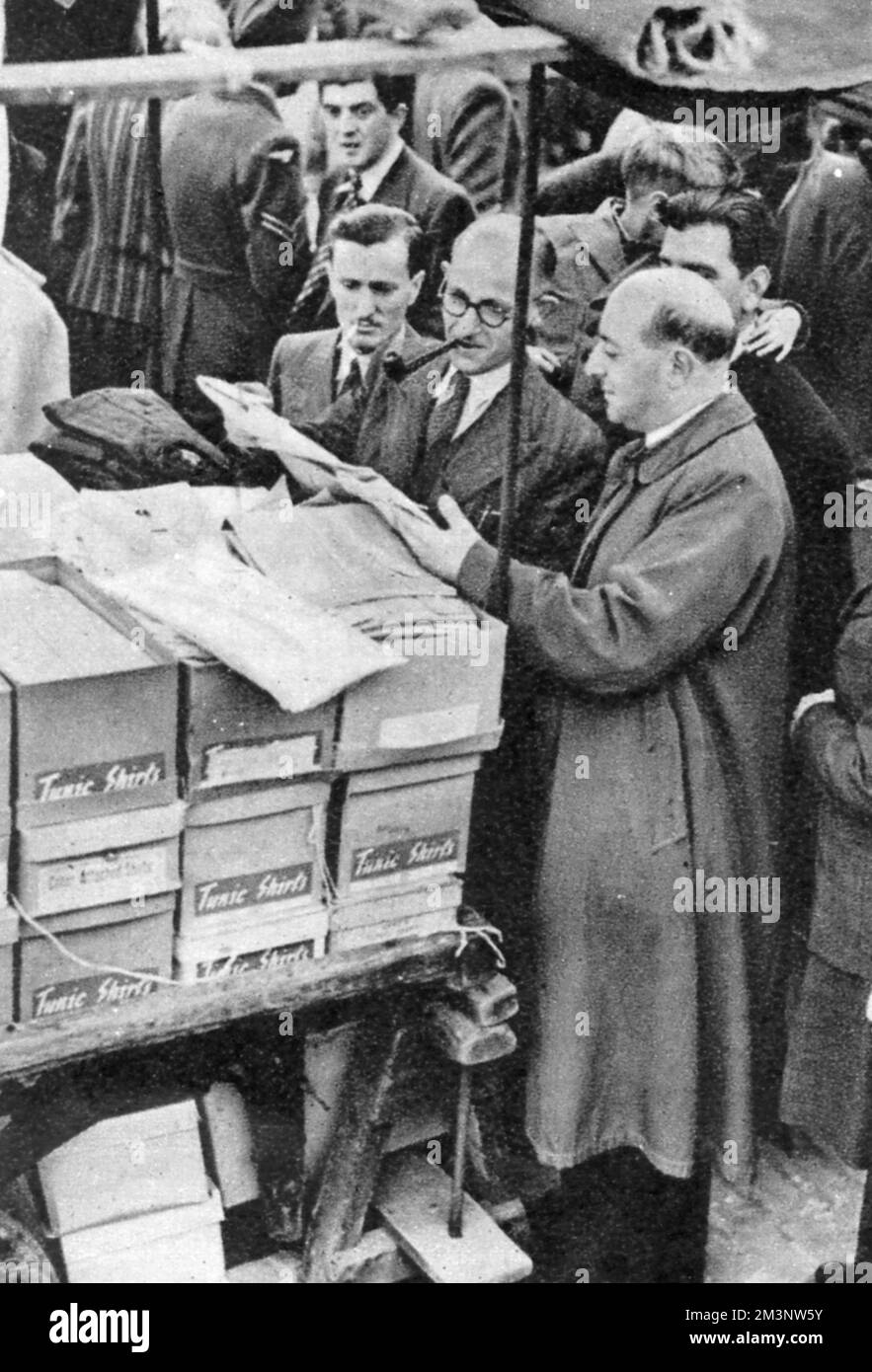 Un venditore al mercato di Petticoat Lane, Londra, mostra il suo stock di camicie a un potenziale acquirente Data: 1945 Foto Stock