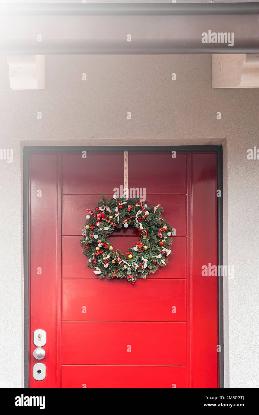 Corona di Natale appesa su una porta di legno rosso Foto Stock
