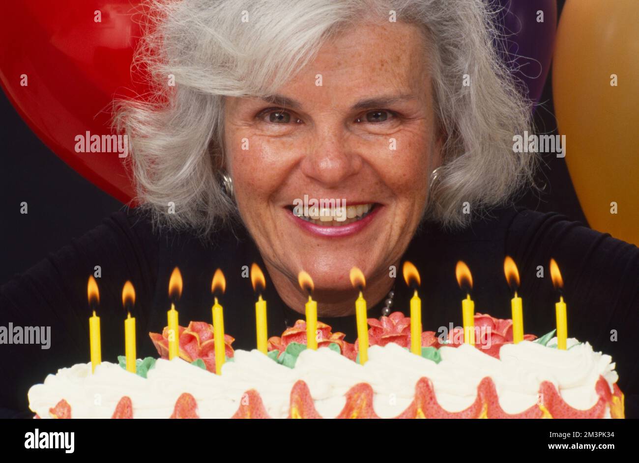 Donna più vecchia dai capelli grigi che si prepara a soffiare le candele sulla sua torta di compleanno Foto Stock