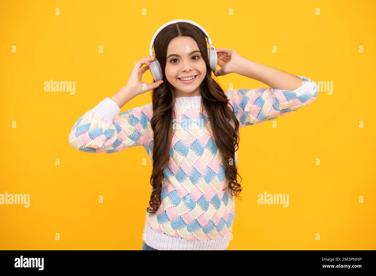 Teen girl in cuffie ascoltare musica. Dispositivo auricolare wireless. I bambini amano la musica in auricolari su sfondo giallo. Foto Stock