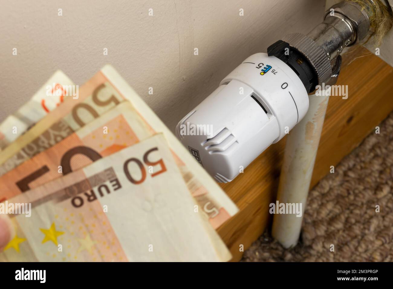 Banconote in euro su batteria radiatore di riscaldamento con termostato regolatore di temperatura. Concetto di costi di riscaldamento costosi e di aumento della bolletta energetica Foto Stock
