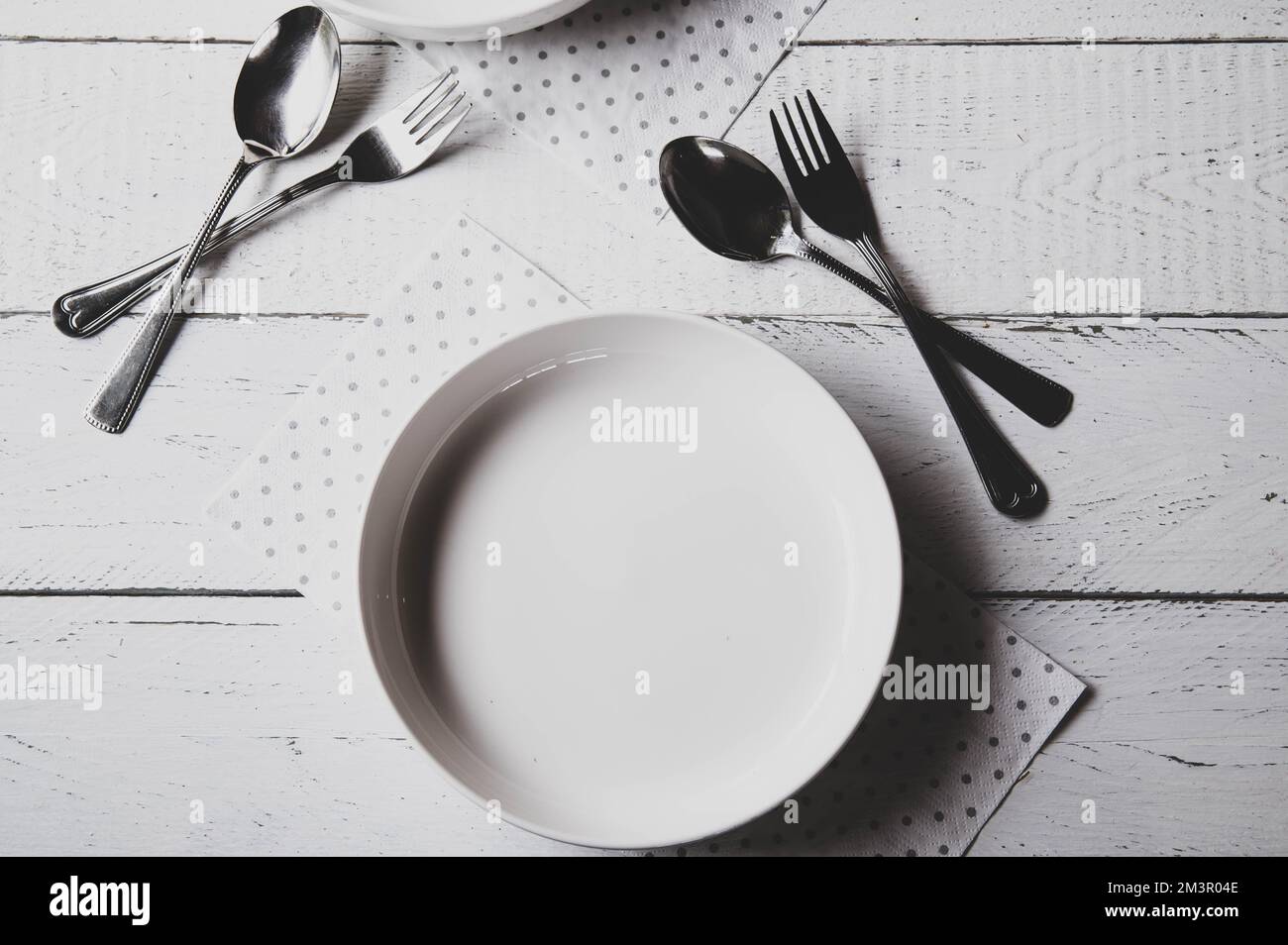 Piatto bianco vuoto con forchetta e cucchiaio su fondo astratto, bianco, opaco Foto Stock