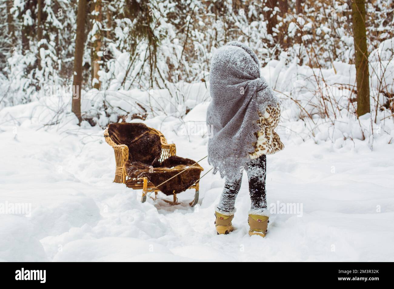 ritratto di bambina in un cappotto di pelliccia e uno scialle caldo porta una slitta sulla passeggiata Foto Stock