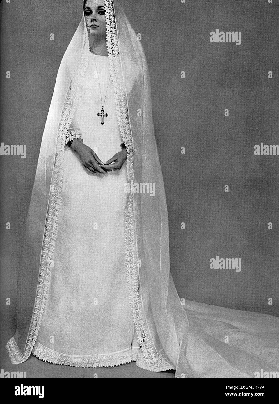 Un abito da sposa in stile camelot e un velo di semplicità monaca in orgdie bianco traslucido con un ampio bordo di pizzo guipure e polsini e orlo, che rifilatura anche il velo e il treno. Di Belinda Belville. Data: 1965 Foto Stock