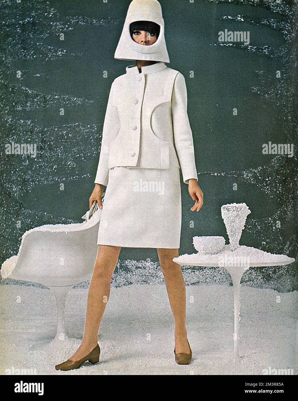 Un vestito garbardine di lana bianca di Cardin. È monopetto con un collare ufficiale e un pannello frontale di intagli semicircolari ed è indossato con un casco da saldatore in feltro bianco. Data: 1966 Foto Stock