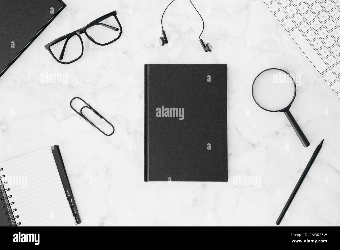 Chiuso diario nero con occhiali auricolari lenti di ingrandimento matita tastiera diario bianco scrivania Foto Stock