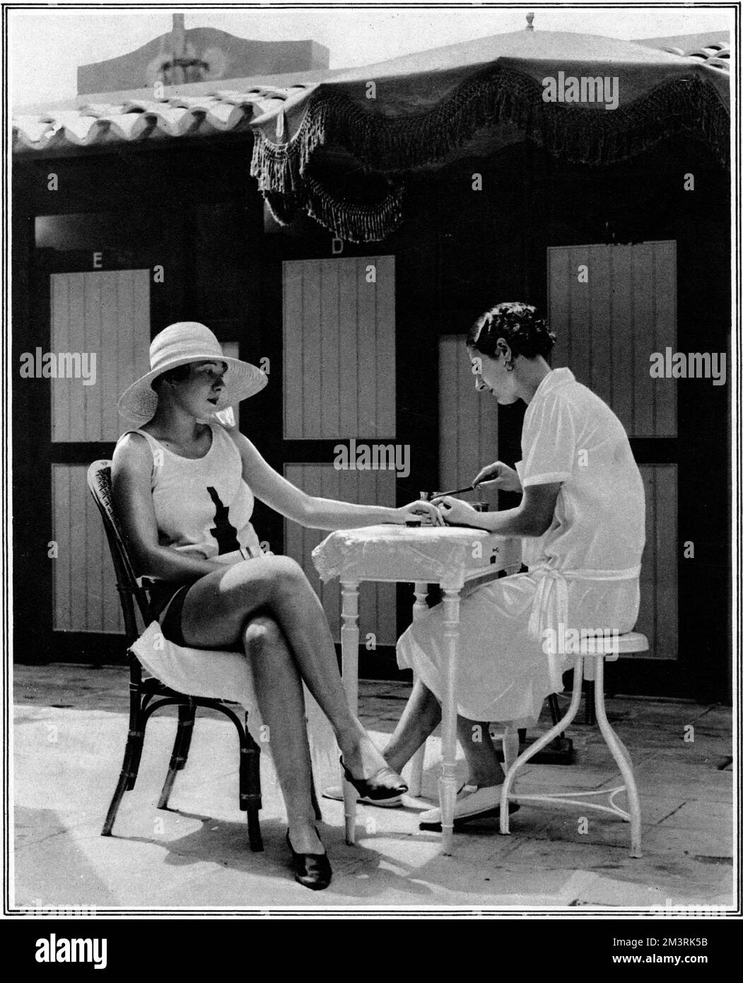 Donna vestita con costume da bagno e cappello largo-brimmed gode di una manicure nella città termale di Juan-les-Pins sulla C&#x134960;d'Azur. 1928 Foto Stock