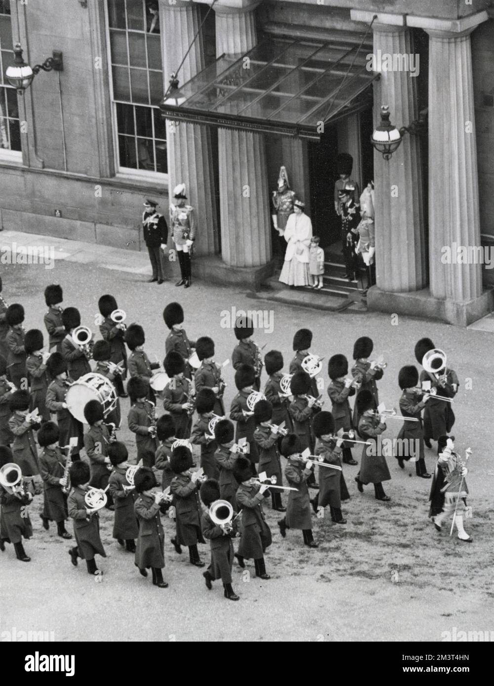 Scena nel piazzale di Buckingham Palace che mostra il Principe Carlo (Re Carlo III) al fianco di sua madre, la Regina Elisabetta II, mentre guardano un passato di marcia della band Guards, Al ritorno di sua Maestà e del Duca di Edimburgo al Palazzo dopo l'apertura dello Stato del Parlamento nel 1952. Foto Stock