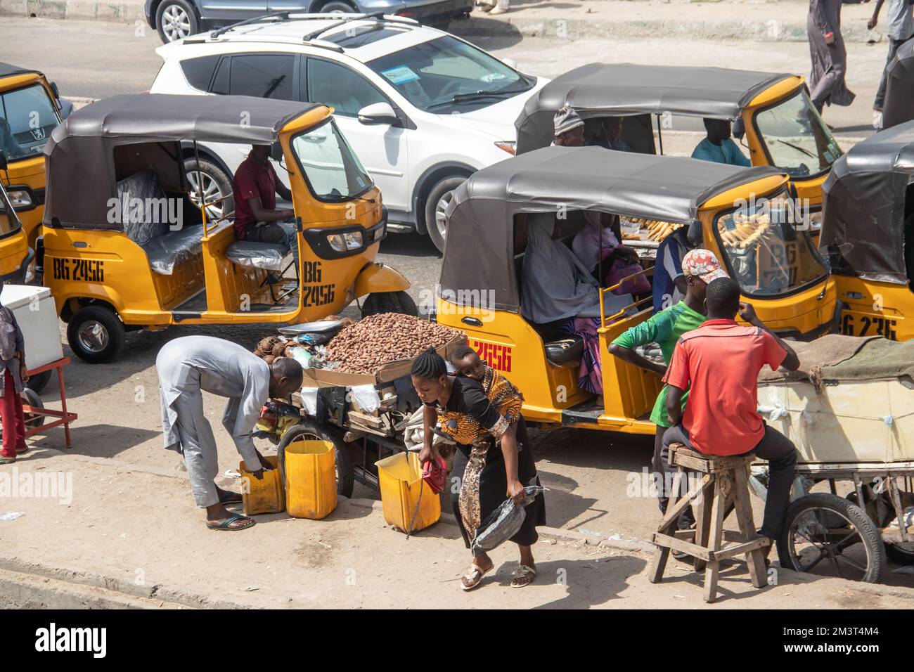 Affollato mercato aperto nelle strade africane con traffico intenso con taxi tuk-tuk e un gruppo di persone affollate che controllano i venditori ambulanti, scenario tipico dell'Africa Foto Stock