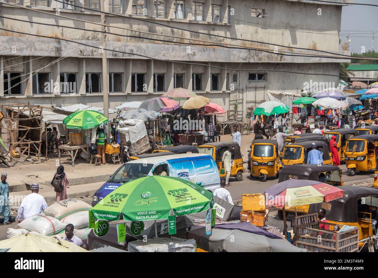 Affollato mercato aperto nelle strade africane con traffico intenso con taxi tuk-tuk e un gruppo di persone affollate che controllano i venditori ambulanti, scenario tipico dell'Africa Foto Stock